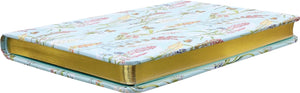 A small journal with a floral and butterfly pattern on a light blue background, featuring gold foil embellishments lying flat on a white background. 