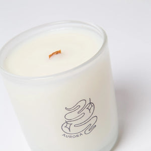 White candle in a translucid glass with "Aurora" written in purple, along with an abstract logo design. The item is shown against a white background.