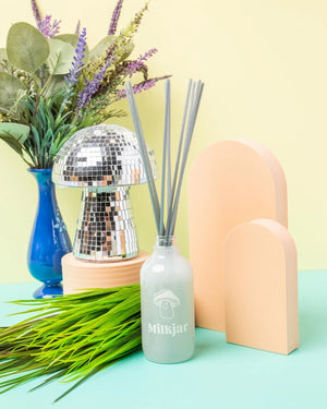 Decorative setup with a mushroom shaped disco ball, plant, and 'Milk Jar' diffuser bottle on a colorful background