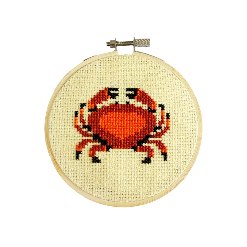 Cross-stitched red and orange crab design on a embroidery hoop with a white background.