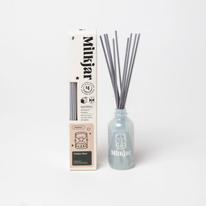 Milkjar diffuser bottle containing reed sticks, placed beside packaging on a white background