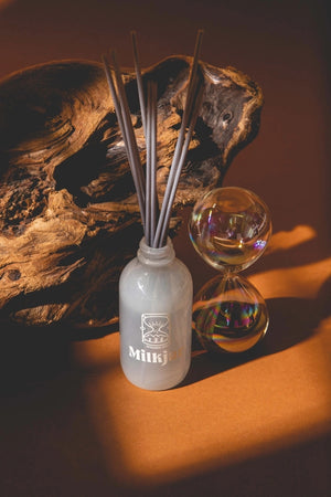 Diffuser bottle with reeds beside a glass sand timer on a wooden surface