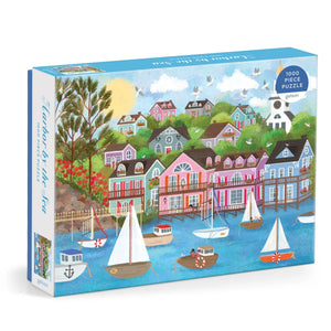 Puzzle box featuring a colourful illustration of a harbour filled with boats. The harbour is surrounded by lots of colourful houses and greenery. The text 'Harbour by the Sea' is printed on the side of the box.