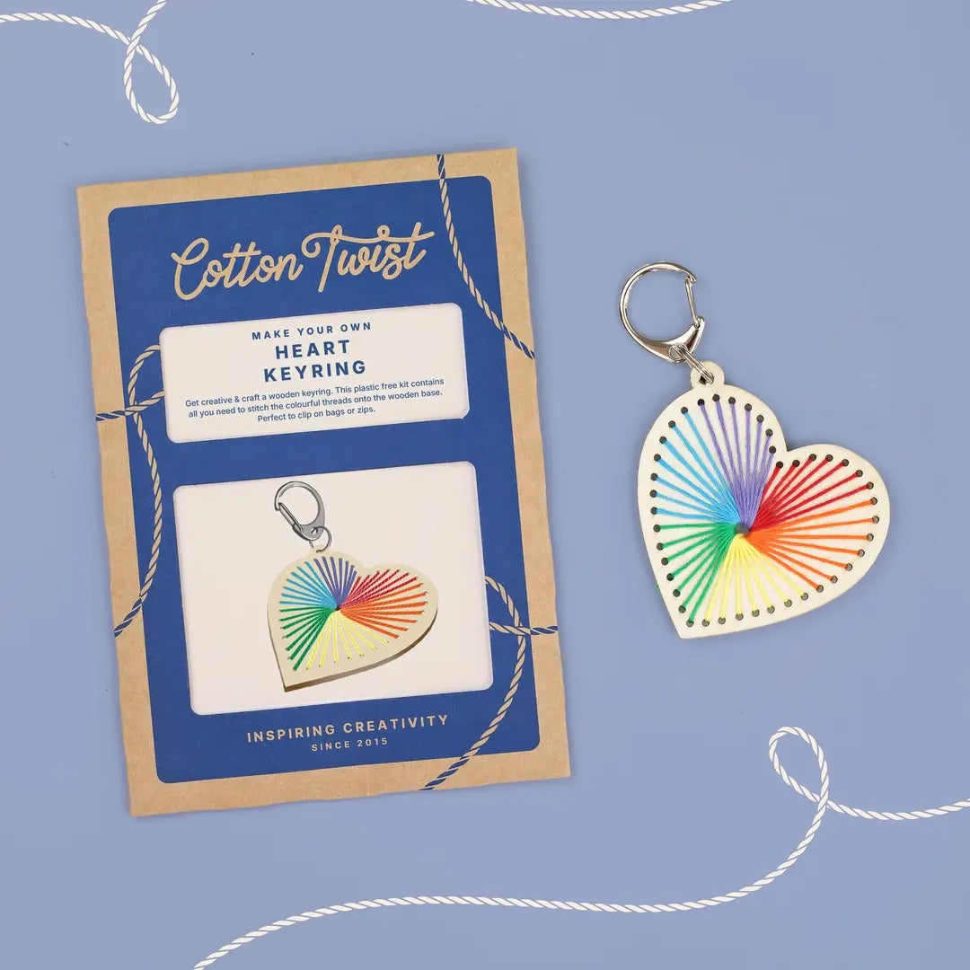 Heart-shaped keyring with a colorful stitched design next to the packaging for a 'Cotton Twist' craft kit on a blue background.