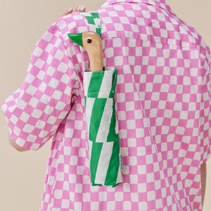 A Person carrying an umbrella with a green and white checkered pattern and a duck head shaped handle.