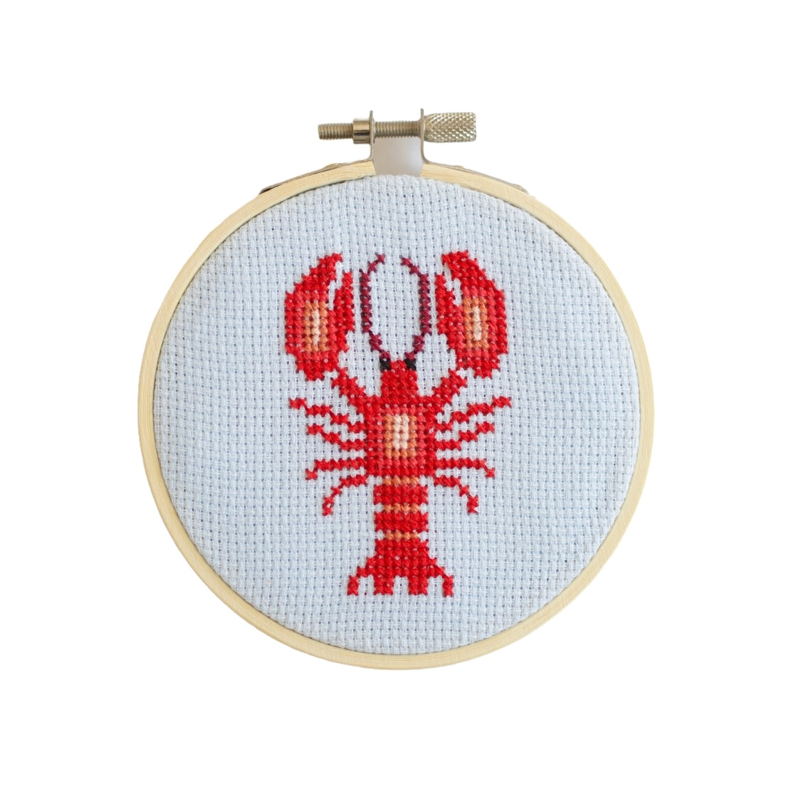 Cross-stitched lobster design contained in a wooden embroidery hoop on a white background.