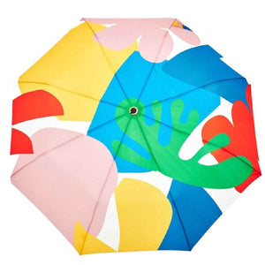 Closeup of the top of an umbrella with a colourful pink, red, yellow and blue abstract pattern and a duck head shaped handle on a white background. 