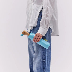 Person holding a closed blue umbrella with a duck head shaped handle on a white background. 