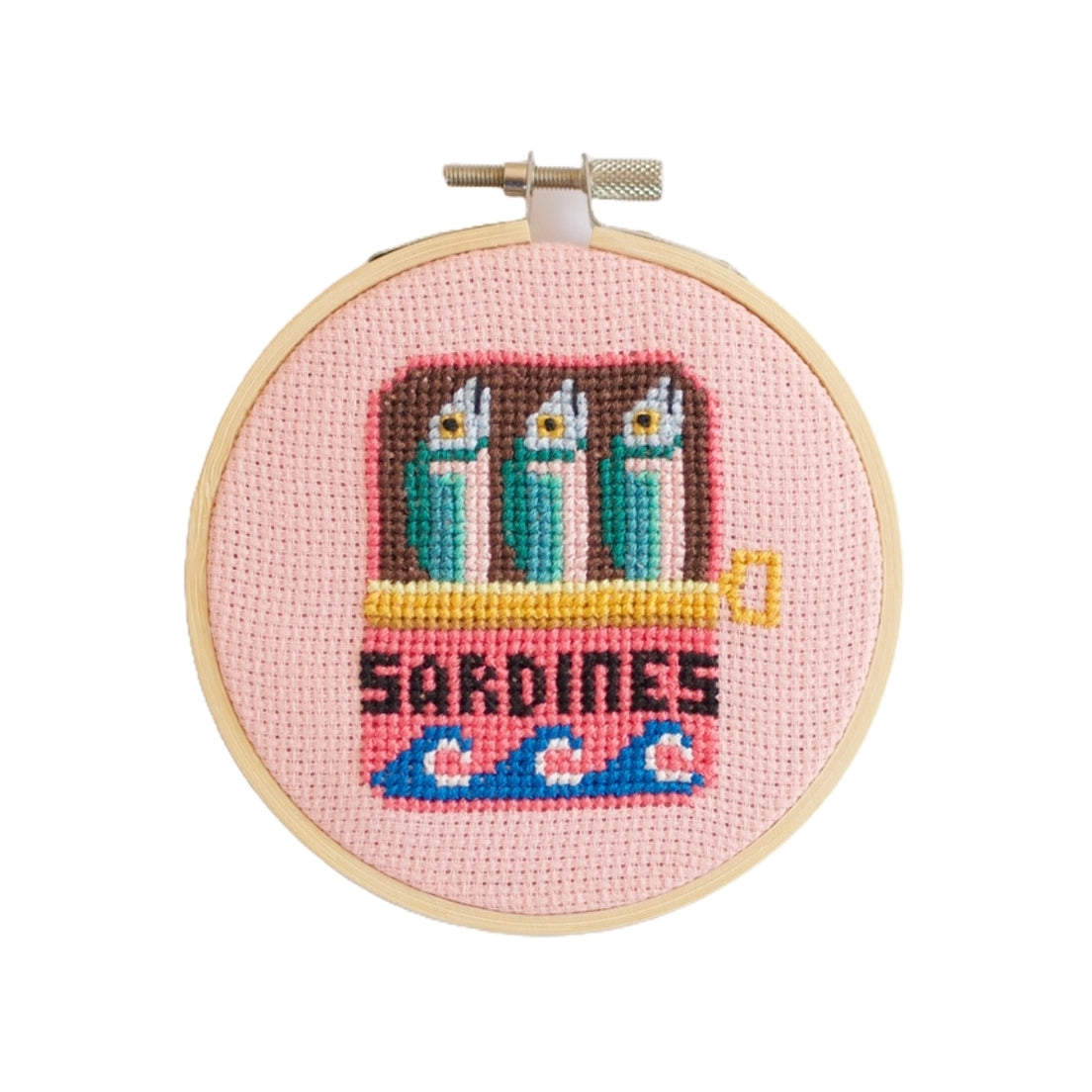Cross-stitched design of sardines in a tin on a pink background, framed in a wooden hoop.