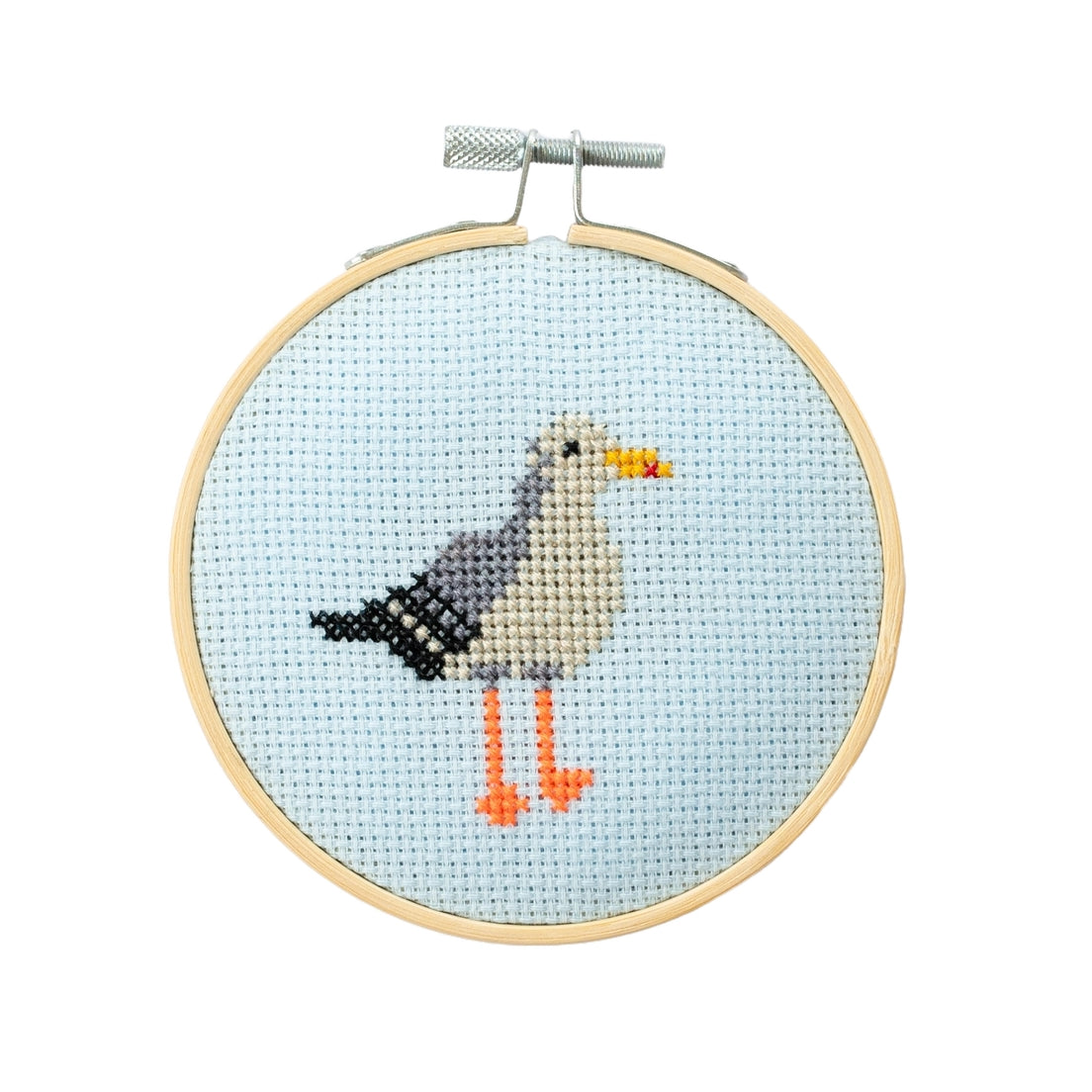 Cross-stitched seagull design contained in a wooden embroidery hoop on a light blue background.
