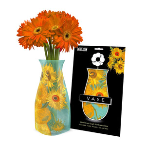 Expandable vase with a yellow, orange and blue floral design based on 'Sunflower Vase' by Van Gogh. The vase is filled with a bouquet of orange flowers and is placed beside it's packaging with Modgy branding.