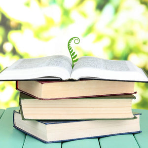 Green fern shaped bookmark sprouting from an open book on a green surface with a blurred natural background