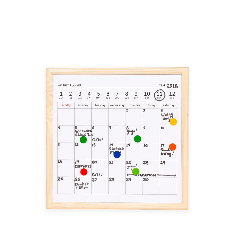 white board calendar with a pale wood frame. both printed and hadnwritten text is seen. kikkerland product on white background