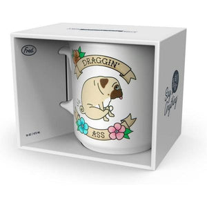 white mug with a stylized design of a pug dragging its butt. two flower-adorned banners frame the dog. on them are written "draggin'" and "ass" in a serif font. The mug sits in a box. 